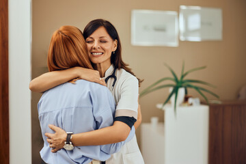 A smiling brunette doctor, hugging her patient, at the clinic, standing at the doctor's office.