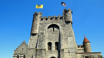 alter Eingangsturm der Burg in Gent mit Ecktürmen und Fahnen unter blauem Himmel