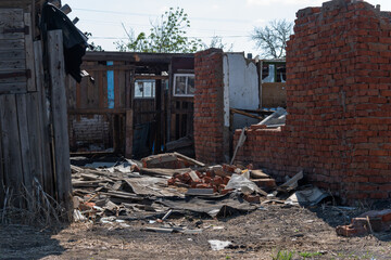 The white walls of an old ruined wooden village house. Broken walls, a ruined roof. Piles of garbage, wooden boards, bricks