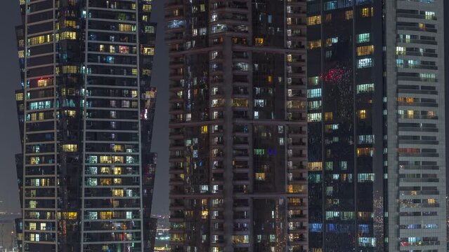 Tall blocks of flats with glowing windows located in residential district of city aerial timelapse. Evening light in rooms in high-rise towers and skyscrapers