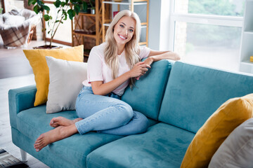 Fototapeta premium Photo of cheerful sweet pretty girl sitting soft sofa baefoot in modern interior room enjoy relax