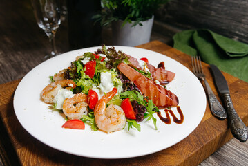A salad with fried shrimp, dressing made with balsamic vinegar, pears soaked in red wine served on a white plate in a restaurant.