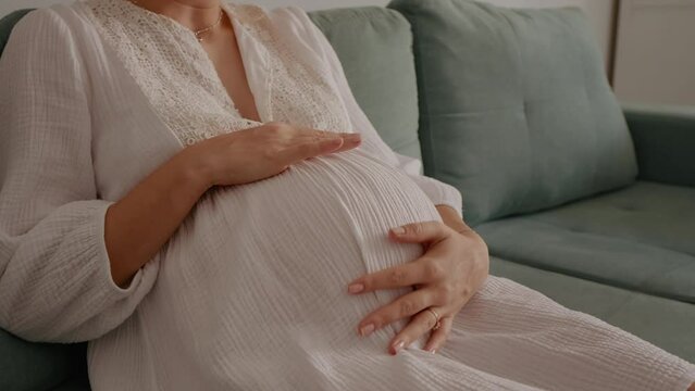 Close up of pregnant woman in early labor feeling sudden contractions sitting on sofa. Unexpected contractions while relaxing at home. Health problems and pregnancy concept.