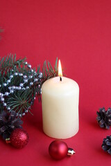 A candle stands on a red background with Christmas tree decorations.