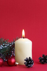  A candle stands on a red background with Christmas tree decorations.