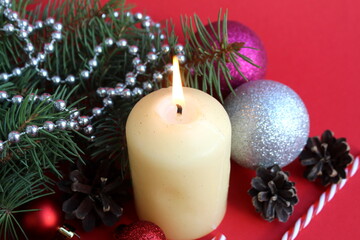 A candle stands on a red background with Christmas tree decorations.