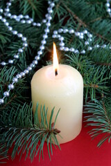 A candle stands on a red background with Christmas tree branches.