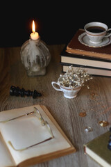 Vintage books, reading glasses, gold pen, hand model, gold jewelry, scented candles, flowers, chess pieces and cup of tea or coffee on the table. Dark academia concept. Selective focus.