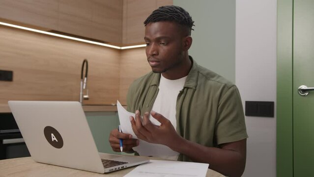 Black Man Working With Documents Using Laptop. 30s entrepreneur managing paperwork invoices taxes bills at home office.