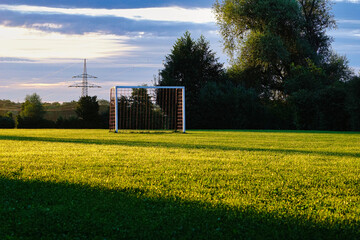 Ein öffentlicher Fußballplatz auf grünem Rasen in ländlicher Umgebung mit Tor. Im Hintergrund Bäume.