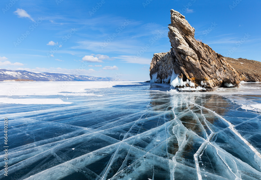 Wall mural Sunny winter day on frozen Baikal Lake. View of the famous Cape Dragon on rocky northern tip of Ogoy Island and the beautiful clear ice with cracks near the cape. Winter travel and outdoor recreation