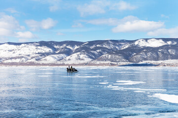 Sunny winter day on frozen Baikal Lake. A couple of tourists travel on the ice of the Small Sea on a snowmobile to Olkhon Island. Winter travel and outdoor recreation