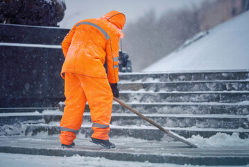 Worker with snow shovel clear snow during blizard, snow removal work. Janitor in uniform with...