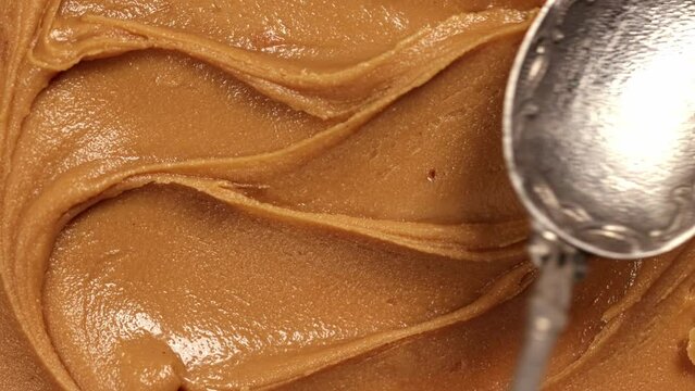Delicious, freshly made, sweet peanut butter. Texture of creamy paste. Wavy movements with retro spoon. Taste. Concept of ingredients, food, sweets
