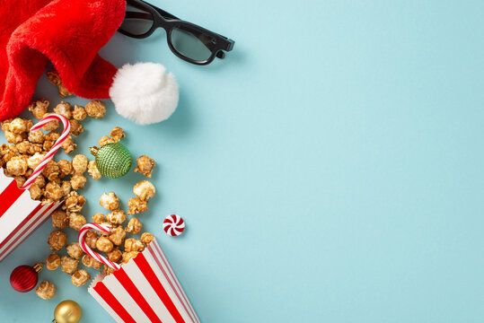 Dive into the world of New Year-themed films. Overhead image of 3D glasses, mouthwatering popcorn, Santa's hat, baubles, sweet treats, candy canes on pastel blue background with space for advertising