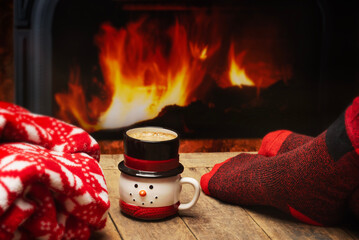 Person sitting next to a fire in warm red socks with coffee in a snowman mug