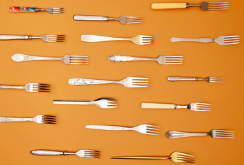 Cutlery. Top view flat lay photo of variety of antique silverware and gold forks arranged over orange studio background.