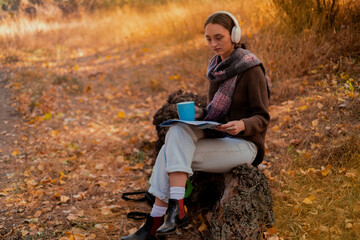 woman with a backpack drinks tea from a cup, dressed in a brown sweater, holds a map in her hands,...