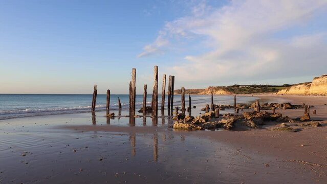 Reflection of wooden jetty remains on the beach coastline.