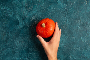 cropped view of male hand near bright orange pumpkin on blue textured surface, thanksgiving concept