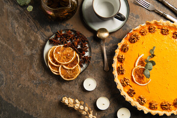 thanksgiving theme, garnished pumpkin pie near candles and orange slices with spices on stone table