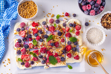 Homemade frozen Yogurt Bark, alternative healthy keto diet ice cream made from greek yogurt, fresh berries, nuts, granola, honey, on baking tray deco. Frozen yoghurt bars with fruit berry toppings