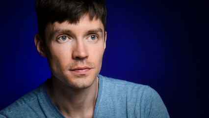 Studio portrait of Caucasian man on dark blue background. Young guy looks away. Copy space. Handsome thin guy in casual clothes.