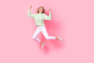 Fototapeta na wymiar Full body photo of overjoyed cheerful lady jumping raise fists empty space isolated on pink color background