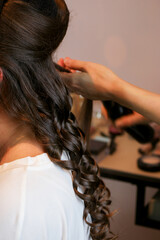 Fototapeta premium Stylist doing curls with irons rod on long brunette hair