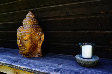 Buddhakopf auf einem Tisch und rechts davon eine weiße Kerze im ländlichen Stil.