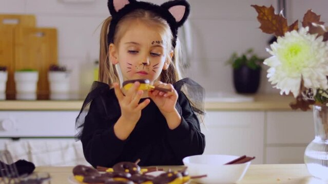 child Halloween costume in the kitchen at home makes donuts with chocolate into spiders, a treat for the holiday, Happy halloween day concept