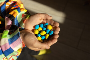 In children's palms lie yellow and blue sweet candies, illuminated by the sun. Ukrainian colors. support for Ukraine. Children ask to stop the war. With love for Ukraine