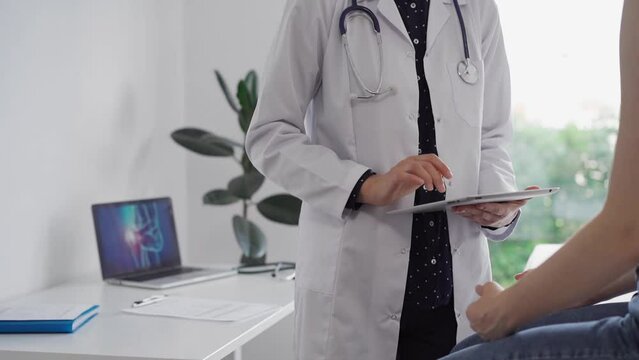 Doctor and patient in the clinic. Orthopedic is using tablet pc for making notes about a young woman's back pain. Medicine rehabilitation concept