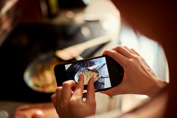 Close up of a woman holding smartphone taking picture of a meal being cooked in the kitchen