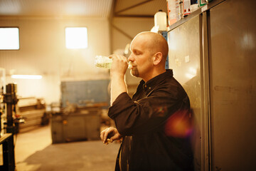 Middle aged mechanic drinking water in the garage