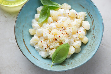 Italian chicche di patate with cheese sauce and basil in a turquoise bowl, middle closeup, horizontal shot on a beige stone surface