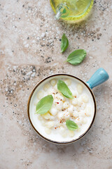 Gnocchi served in cheese sauce with fresh green basil, above view on a beige granite background, vertical shot