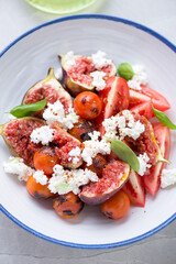 Close-up of salad with tomatoes, fresh fig fruits, goat cheese and green basil, vertical shot, selective focus