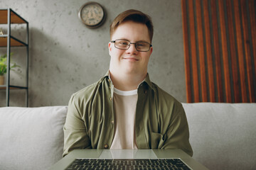 Young IT man with down syndrome wearing casual clothes work hold use laptop pc computer sit on grey...
