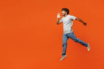 Fototapeta na wymiar Full body young fun Indian man he wears t-shirt casual clothes jump high run scream sharing hot news about sales discount with hands near mouth isolated on orange red color background studio portrait.