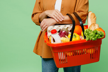 Close up cropped photo shot of caucasian european woman wearing brown shirt casual clothes hold shopping basket bag with food products isolated on plain green background. Delivery service from shop.