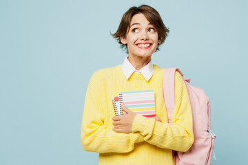 Obraz premium Young cheerful fun woman student wear casual clothes yellow sweater backpack bag hold books looking aside on area copy space isolated on plain blue background. High school university college concept.