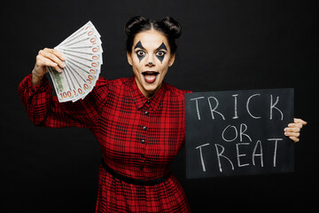Young woman with Halloween makeup face art mask wear clown costume red dress hold card trick or...