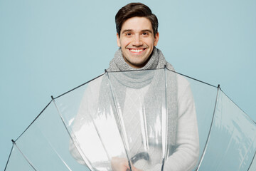 Young smiling ill sick man wear gray sweater scarf hold umbrella look camera isolated on plain blue...