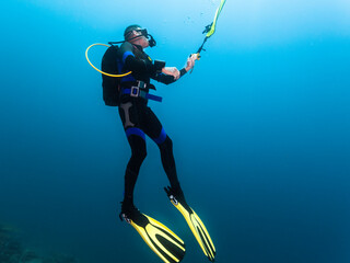 Male scuba diver underwater hanging in the blue deploying up his DSMB deflatable surface marker...
