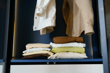Neatly stacked clothes on a shelf in the closet and shirts on hangers. Concept of seasonal wardrobe...