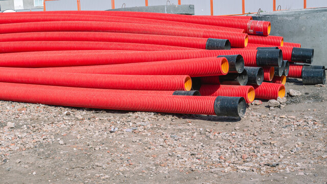 Red pipes made of polyvinyl chloride. Plastic corrugated pipes for carrying out communications during construction and repair. Laying pipes in trenches.