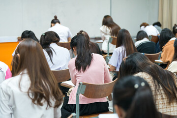 Selective focus high school or university students concentrate writing on paper answer sheet for final exam in the classroom