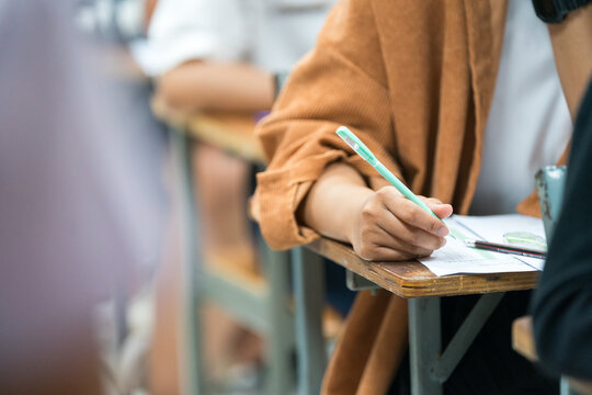 Selective focus high school or university students concentrate writing on paper answer sheet for final exam in the classroom