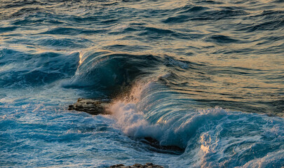 Magical breaking wave texture with colorful patterns reflecting from the sunset in Ikaria, Greece
